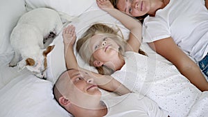 Family with two children lie on a white big bed