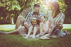 family with two children in meadow using laptop and digita photo