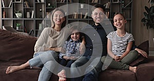 Family with two children sit on sofa look at camera