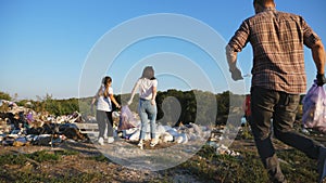 Family with two kids jogging with garbage bags at lawn and throwing them on landfill at nature. Young parents set the