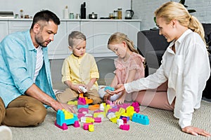 family with two kids sitting on carpet and playing with colorful blocks