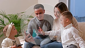 Family with two kids speaking with grandmother on web camera making hi sign.