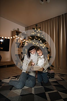 Family of two mother and little cute child girl with magic gift at home near Christmas tree.