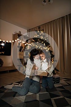 Family of two mother and little cute child girl with magic gift at home near Christmas tree.