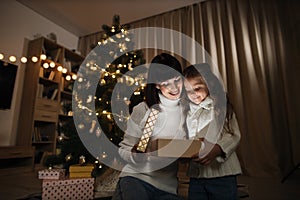 Family of two mother and little cute child girl with magic gift at home near Christmas tree.