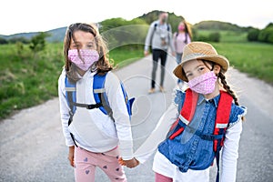 Family with two small daughters on trip outdoors in nature, wearing face masks.