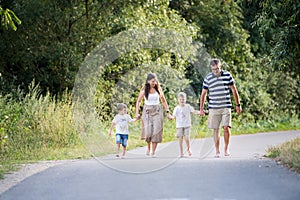 A family with two small sons walking barefoot on a road in park on a summer day.