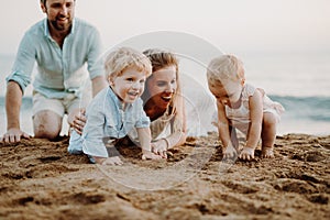 A family with two toddler children lying on sand beach on summer holiday.