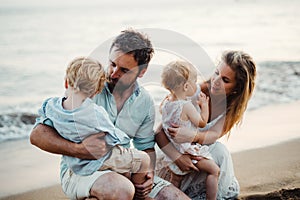 A family with two toddler children sitting on sand beach on summer holiday.