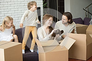 Family unpacking boxes, kids playing on sofa in new home