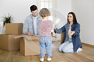 Family Unpacking Cardboard Box With Belongings After Moving To New Home