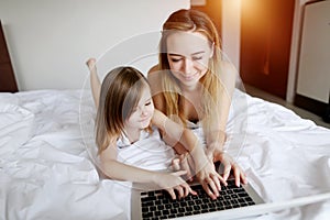 Family using laptop laying on white bed woman and kid girl daughter with sunshine