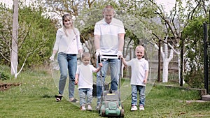 Family using lawn-mower and cutting grass together in village