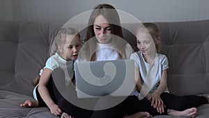 Family is using mobile devices together sitting on sofa during weekend at home. mother and two kids daughter holding