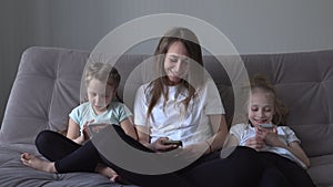 Family is using mobile devices together sitting on sofa during weekend at home. mother and two kids daughter holding