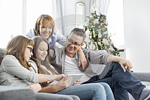 Family using tablet PC on sofa with Christmas tree in background