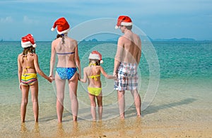 Family vacation on Christmas and New Year holidays, happy parents and children in santa hats have fun on beach