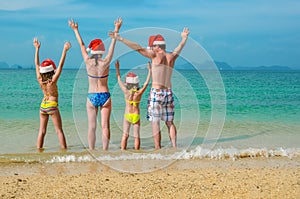 Family vacation on Christmas and New Year holidays, happy parents and children in santa hats have fun on beach