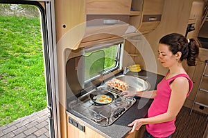Family vacation, RV holiday trip, camping, happy smiling woman cooking in camper, motorhome interior