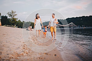 Family vacation in summer. Young Caucasian family foot walking barefoot sandy beach, shore river water. Dad mom holding hands two
