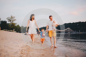 Family vacation in summer. Young Caucasian family foot walking barefoot sandy beach, shore river water. Dad mom holding hands two
