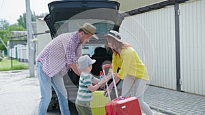 Family vacations, happy husband and joyful wife with their little boys put travel suitcases in trunk of car for