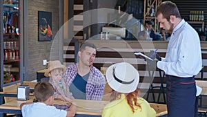 Family vacations, happy parents with their young male children enjoy joint rest in cafe order