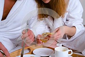Young couple in bathrobes having a breakfast together in bed in hotel room.