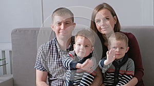 Family video portrait of mom, dad and two twins brothers toddlers. They are siting on the sofa and looking at camera