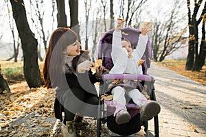 Family walk in autumn park at sunny day. Outdoor shot of pretty young mother playing with her little baby girl in the