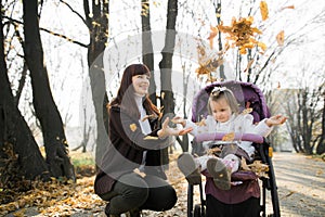 Family walk in autumn park at sunny day. Outdoor shot of pretty young mother playing with her little baby girl in the