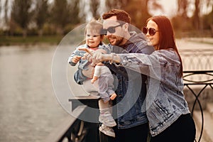 Family walk, father and mother hold daughter in their arms, family walks by the river, sunset, mother points with her hand