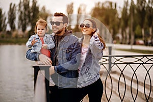 Family walk, father and mother hold their daughter in their arms, the family walks along the embankment of the river, sunset, mom