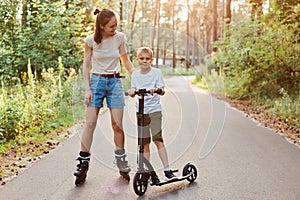 Family walk and rest in the summer day, mom riding roller skates and her son skates on a scooter in a recreation park, spending