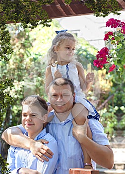 Family on a walk in the summer. Father, son and daughter are having fun in nature. Little daughter sitting on dad`s shoulders.