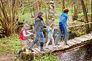 Family Walking Across Wooden Bridge Over Stream In Forest