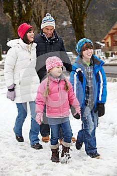 Family Walking Along Snowy Street In Ski Resort