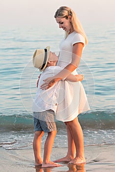 Family walking on the evening beach during sunset.Mother and son embracing, looking at the sea.