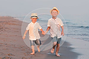 Family walking on the evening beach during sunset.Two brothers in straw hats.