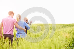 Family Walking In Field Carrying Young Baby Son