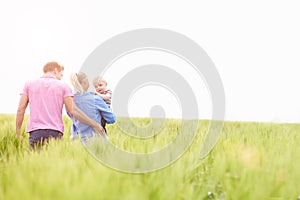 Family Walking In Field Carrying Young Baby Son