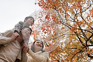 Family walking through the park in the autumn, little boy sitting on his fathers shoulders