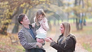 Family walking in park, father carries daughter in his arms and mom tickles her