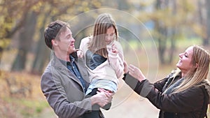 Family walking in park, father carries daughter in his arms and mom tickles her