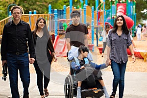 Family walking past playground with disabled son in wheelchair