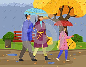 Family walking in the rain with umbrella and wearing raincoats in the city park in autumn season