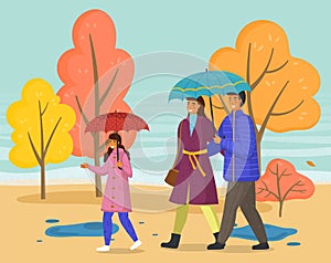 Family walking in the rain with umbrella and wearing raincoats in the city park in autumn season