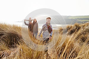 Family Walking Through Sand Dunes On Winter Beach