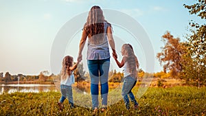 Family walking by summer river at sunset. Mother and her daughters having fun outdoors