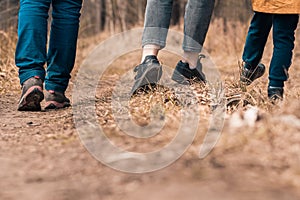 Family walks with children in forest path. Rear view on legs and shoes hikers. Walking boots and sneakers on ground and dry grass